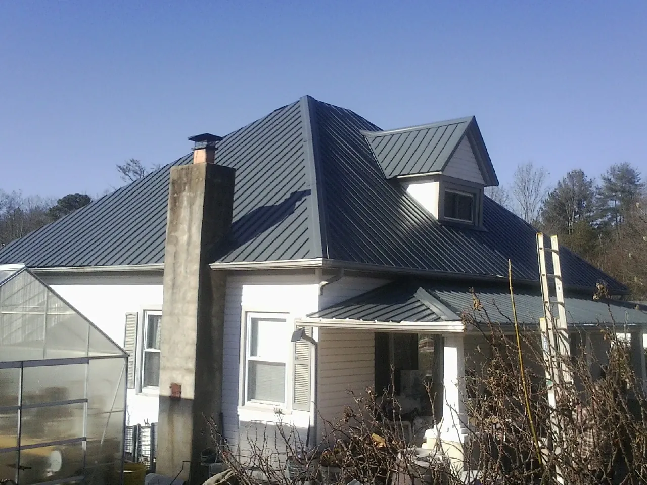 Dark blue standing seam metal roof on a white farmhouse with dormer — Slate & Tile Roof Repair by Roofing Brothers in Glen Aubrey