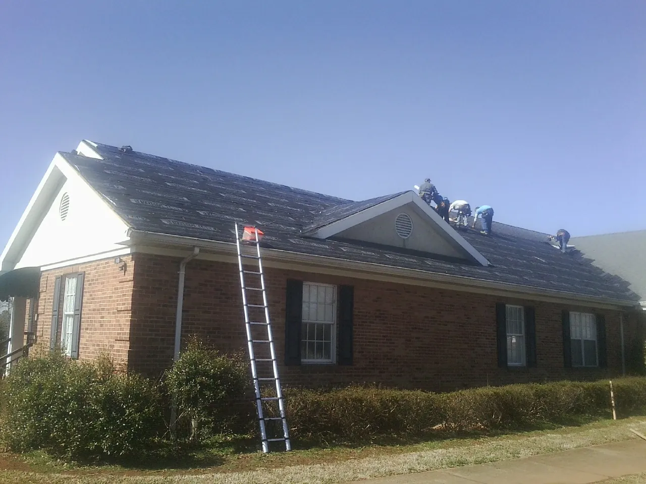 Crew tearing shingles off a brick ranch roof with a ladder set — Metal Roof Repair work by our crew in Glen Aubrey