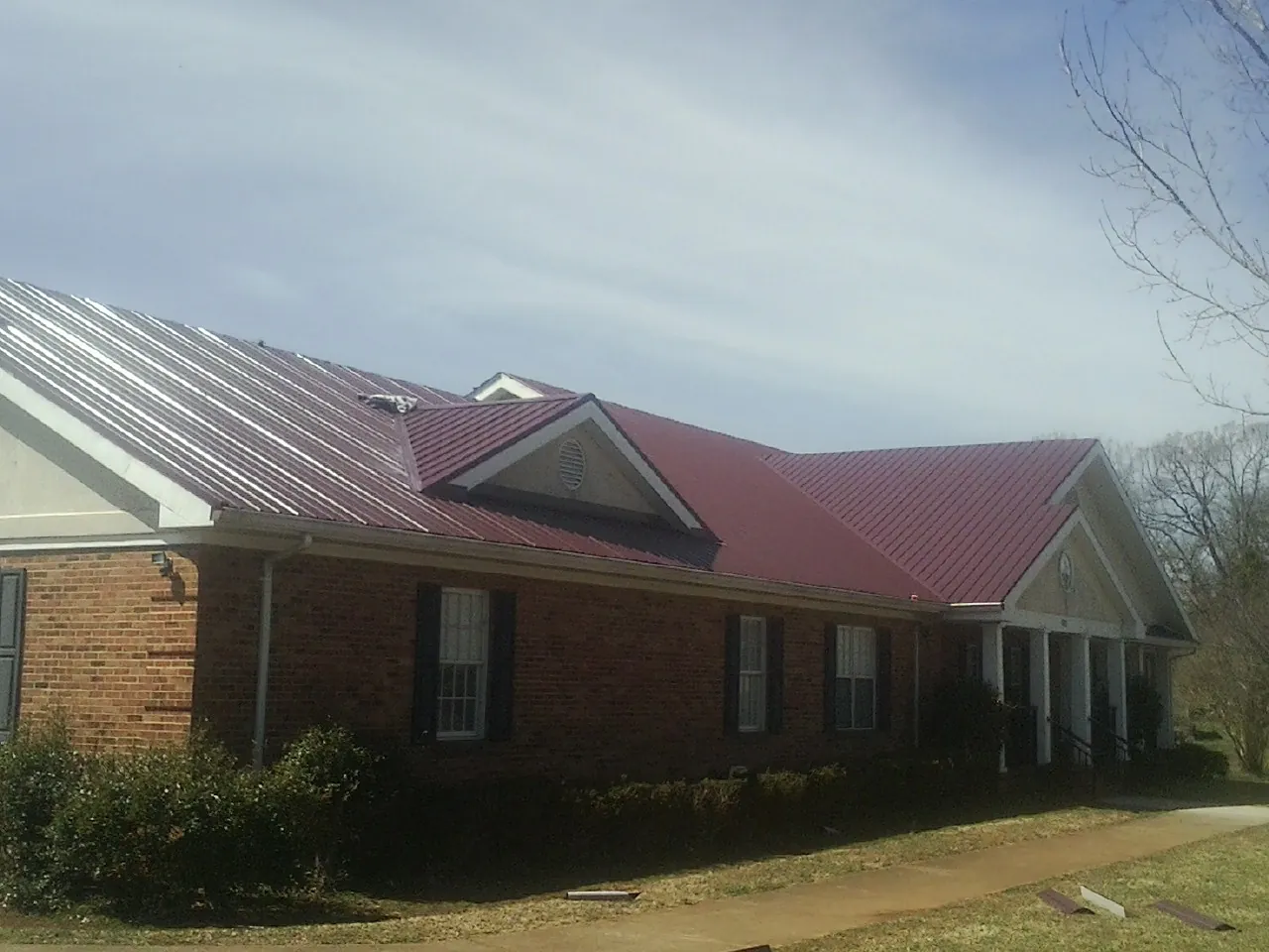 Red metal roof with gabled entries on a long brick building, from a Hail Damage Roof Repair job in Glen Aubrey