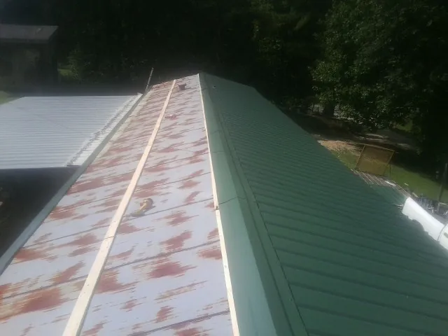 Old rusted panels beside newly installed green metal roofing — Wind Damage Roof Repair by Roofing Brothers in Glen Aubrey