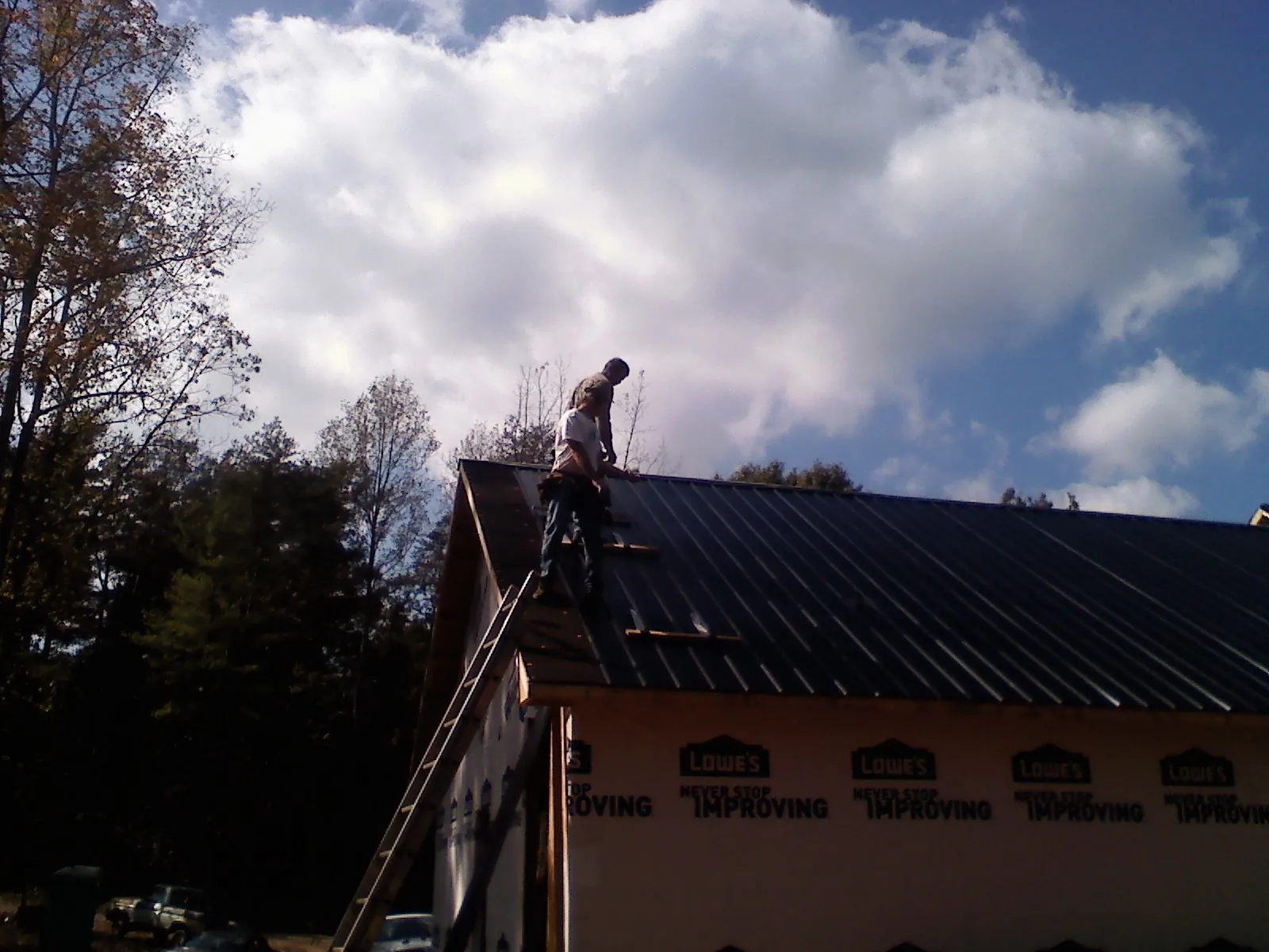 Roofer fastening dark metal panels high against a cloudy sky, from a Roof Inspection job in Glen Aubrey