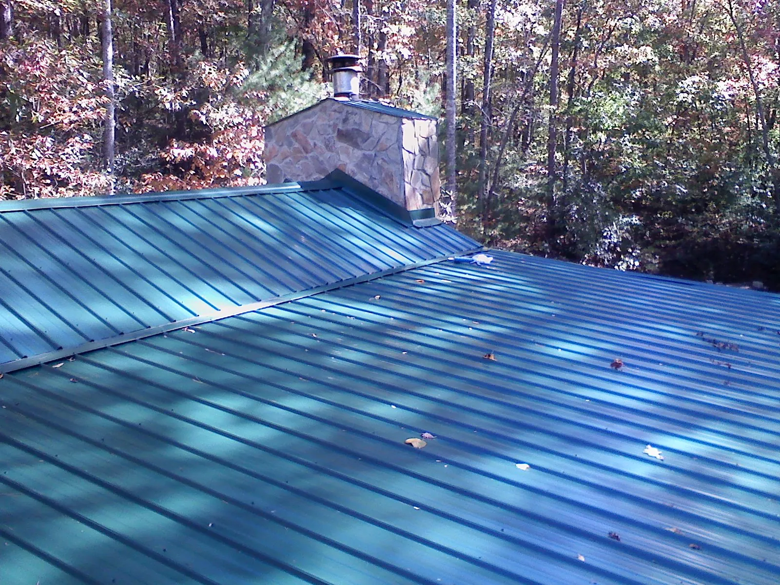 New green metal roof and stone chimney surrounded by autumn woods in Glen Aubrey