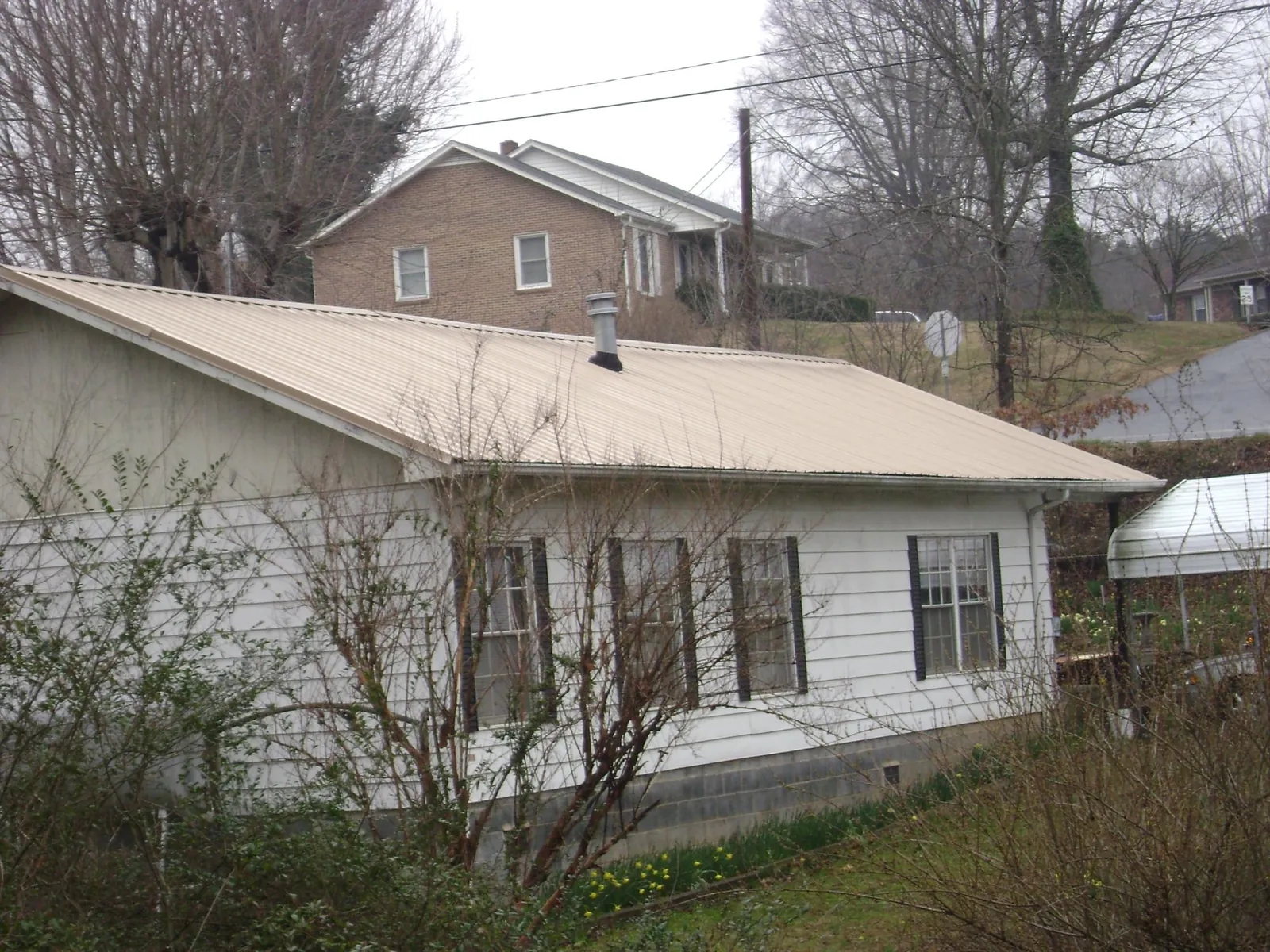 Tan metal roof on a white sided house set into a hillside — Commercial Roofing by Roofing Brothers in Glen Aubrey
