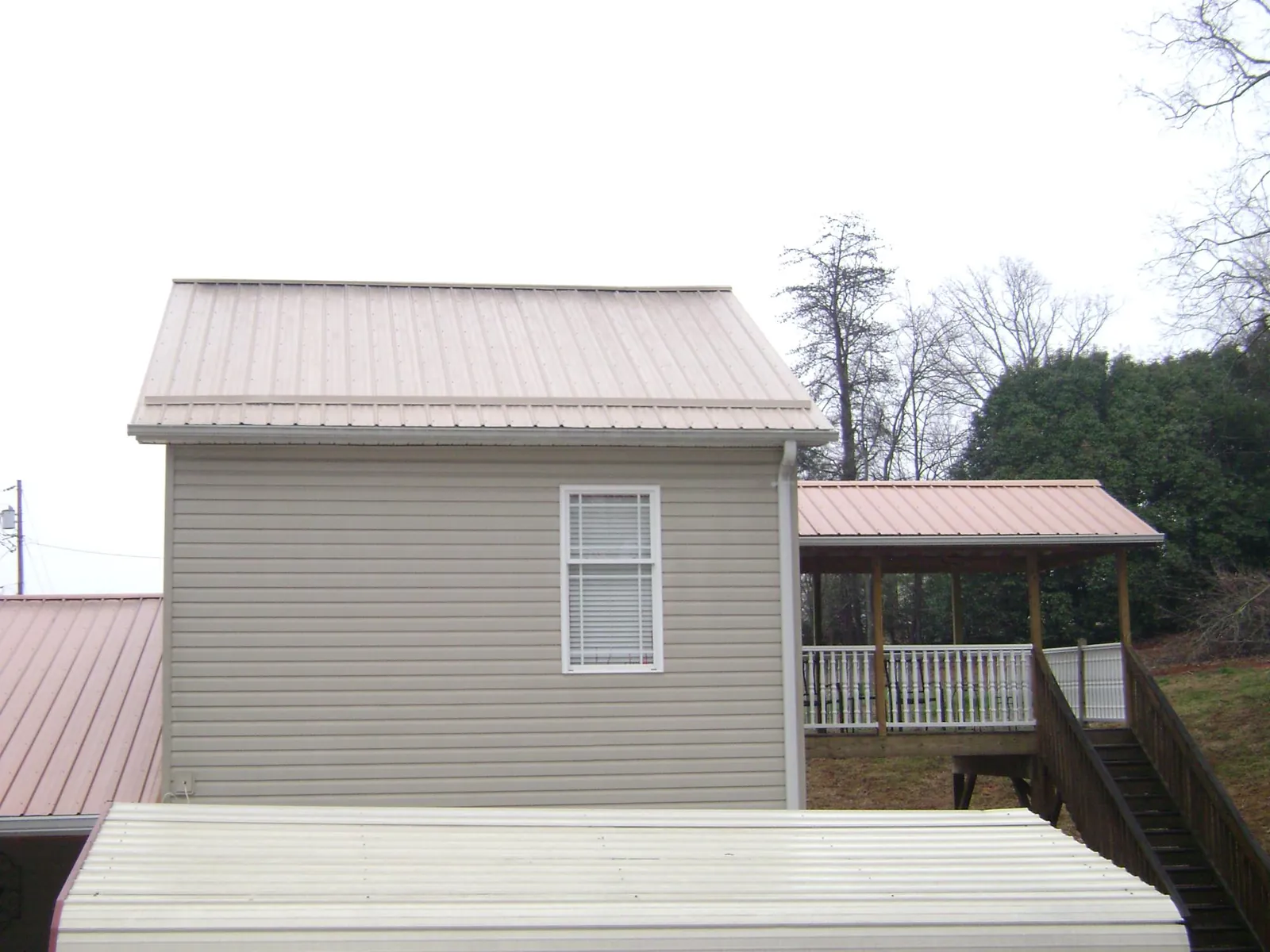 Tan metal roofs on a two story addition and attached porch, from a Roof Replacement job in Glen Aubrey